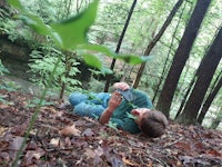 a boy laying on the ground in the woods